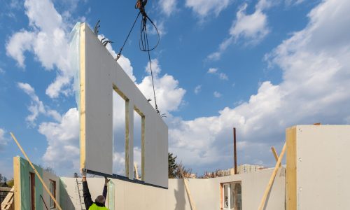 Construction new and modern modular house from composite sip panels. Worker man in uniform wear working on building development industry of energy efficient property against blue sky background